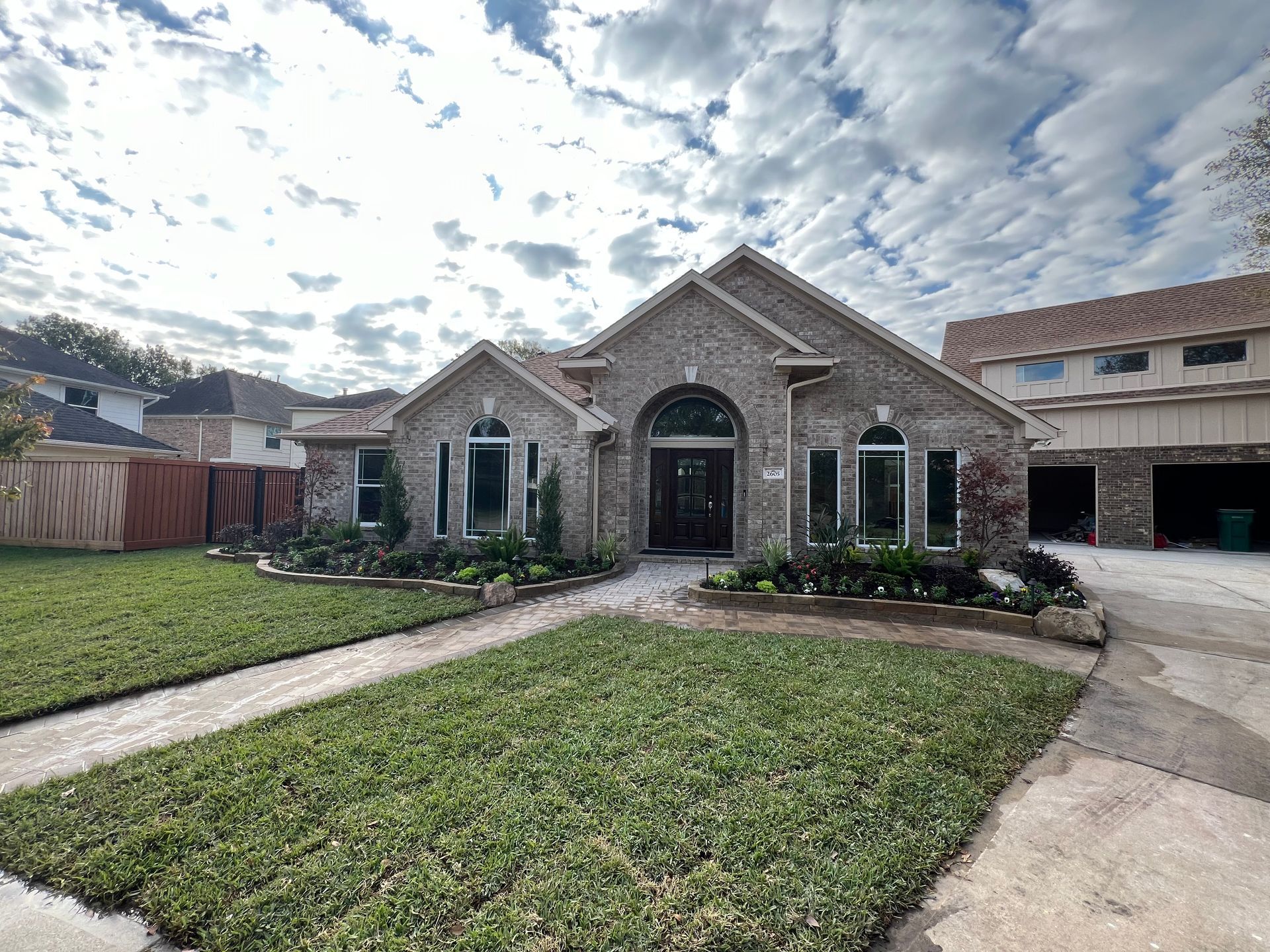 Stone-front single-story house with manicured lawn, curved walkway, and cloudy sky