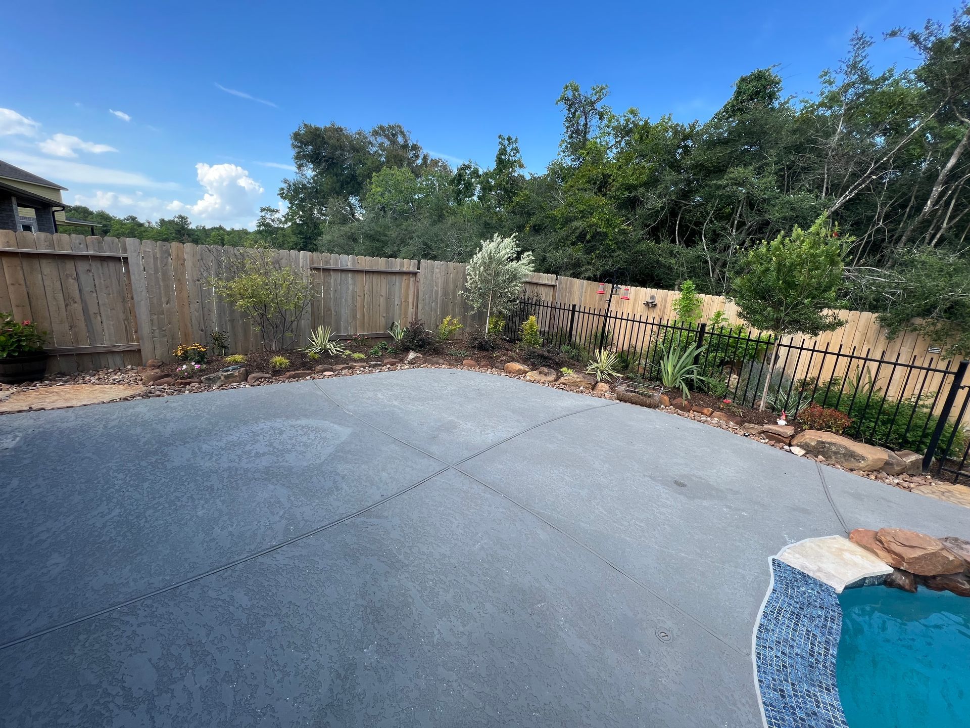 Empty backyard patio with concrete slab, wooden fence, trees, and blue sky