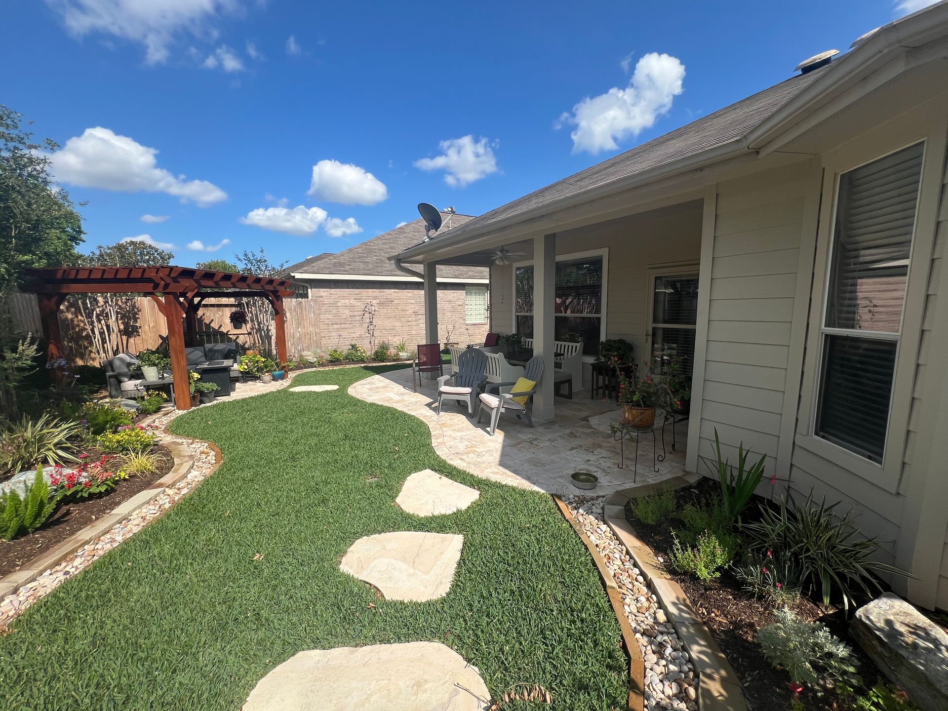 Backyard patio with curved stepping-stone path, green lawn, flower beds, and covered seating area