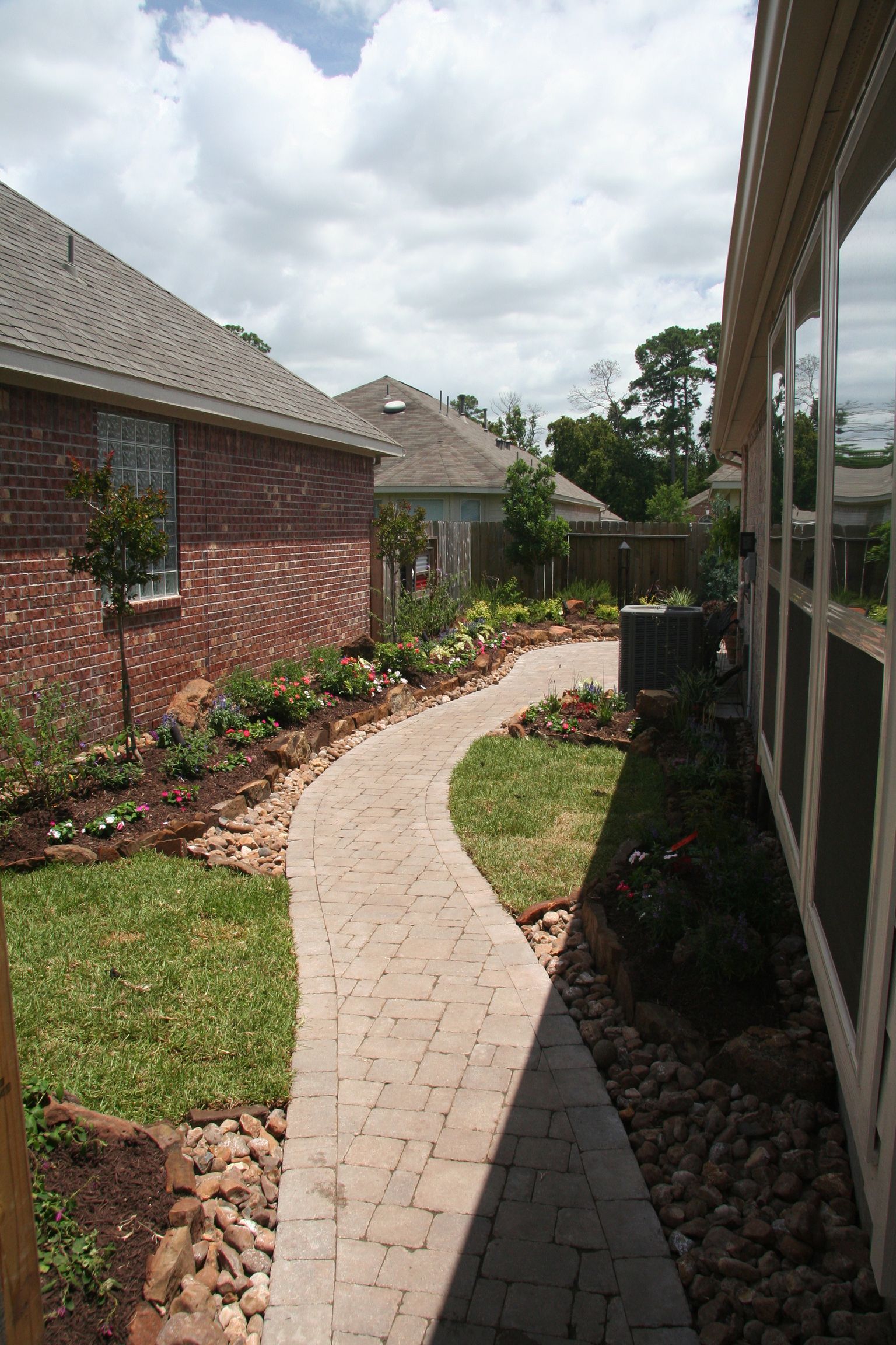 Curved brick walkway between a red brick house and screened porch under a cloudy sky