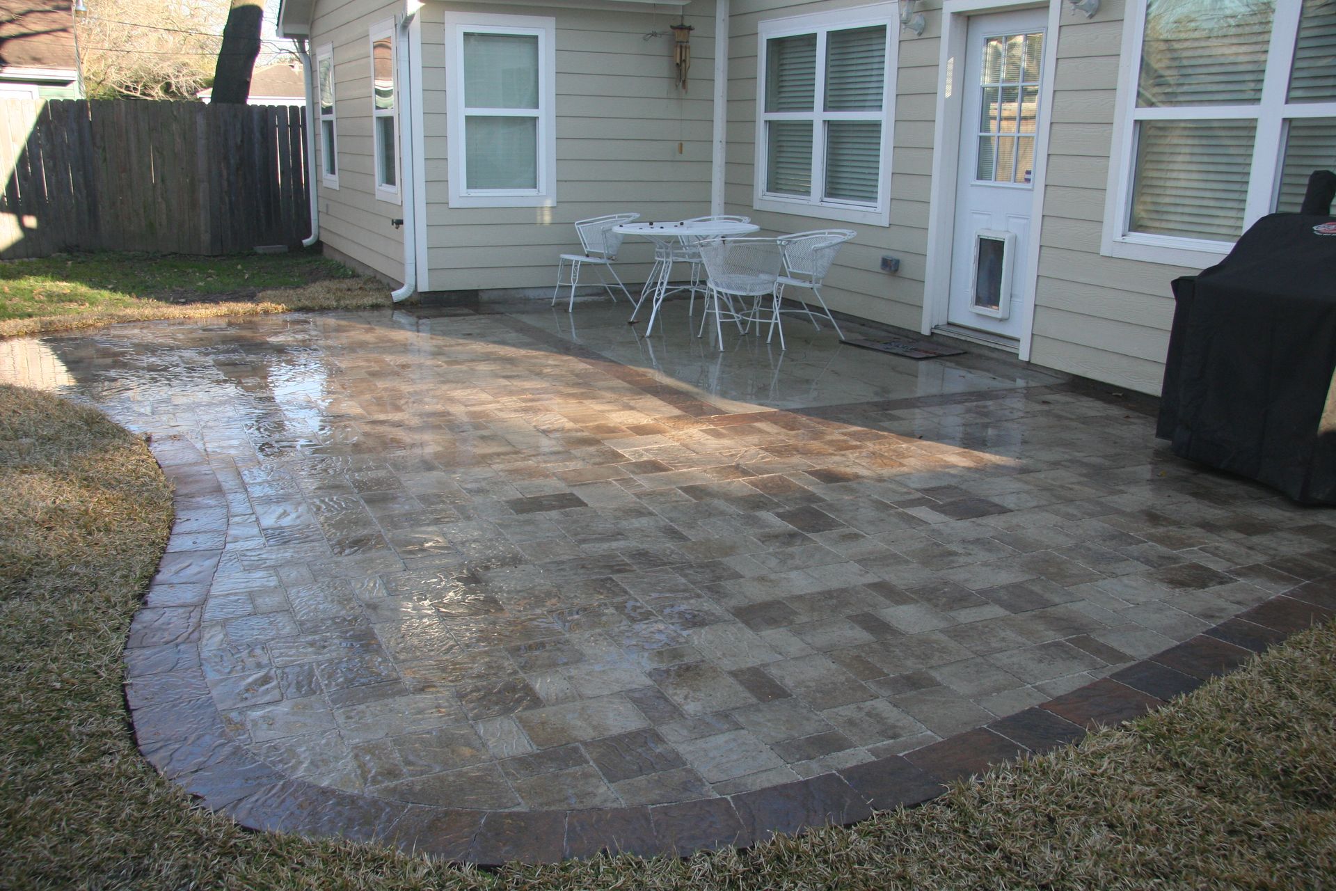 Backyard patio with brick pavers, outdoor dining set, and a grill beside a house