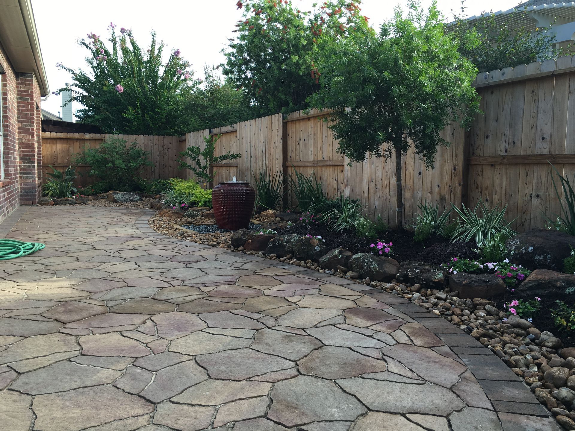 Stone patio beside a wooden fence and landscaped garden with shrubs and flowers