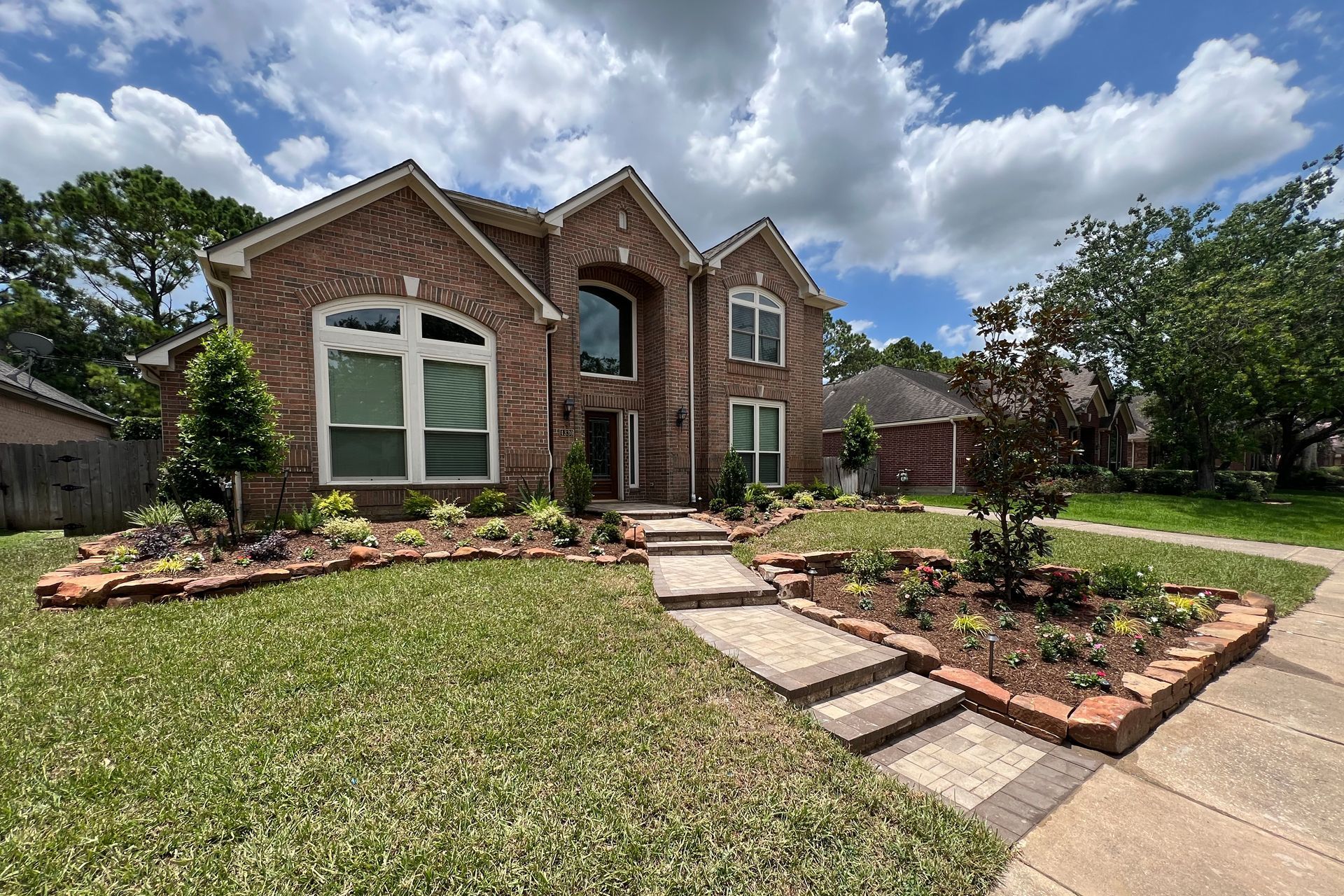Brick suburban house with landscaped front yard, stone walkway, and cloudy sky