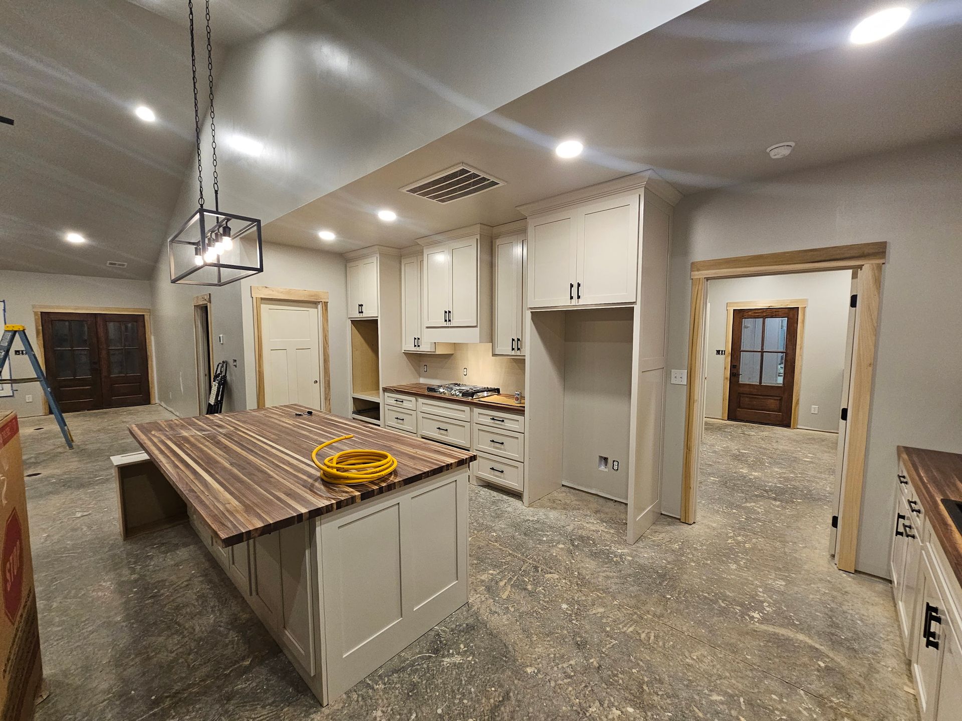 Kitchen under construction; island with wood countertop, light cabinets, and open doorways