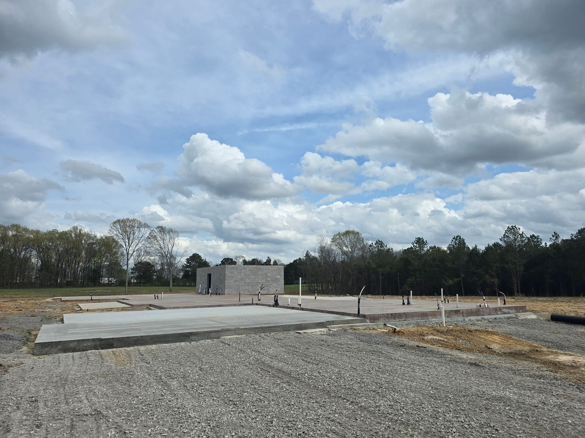 Construction site with a concrete foundation, cinder block building, and cloudy sky