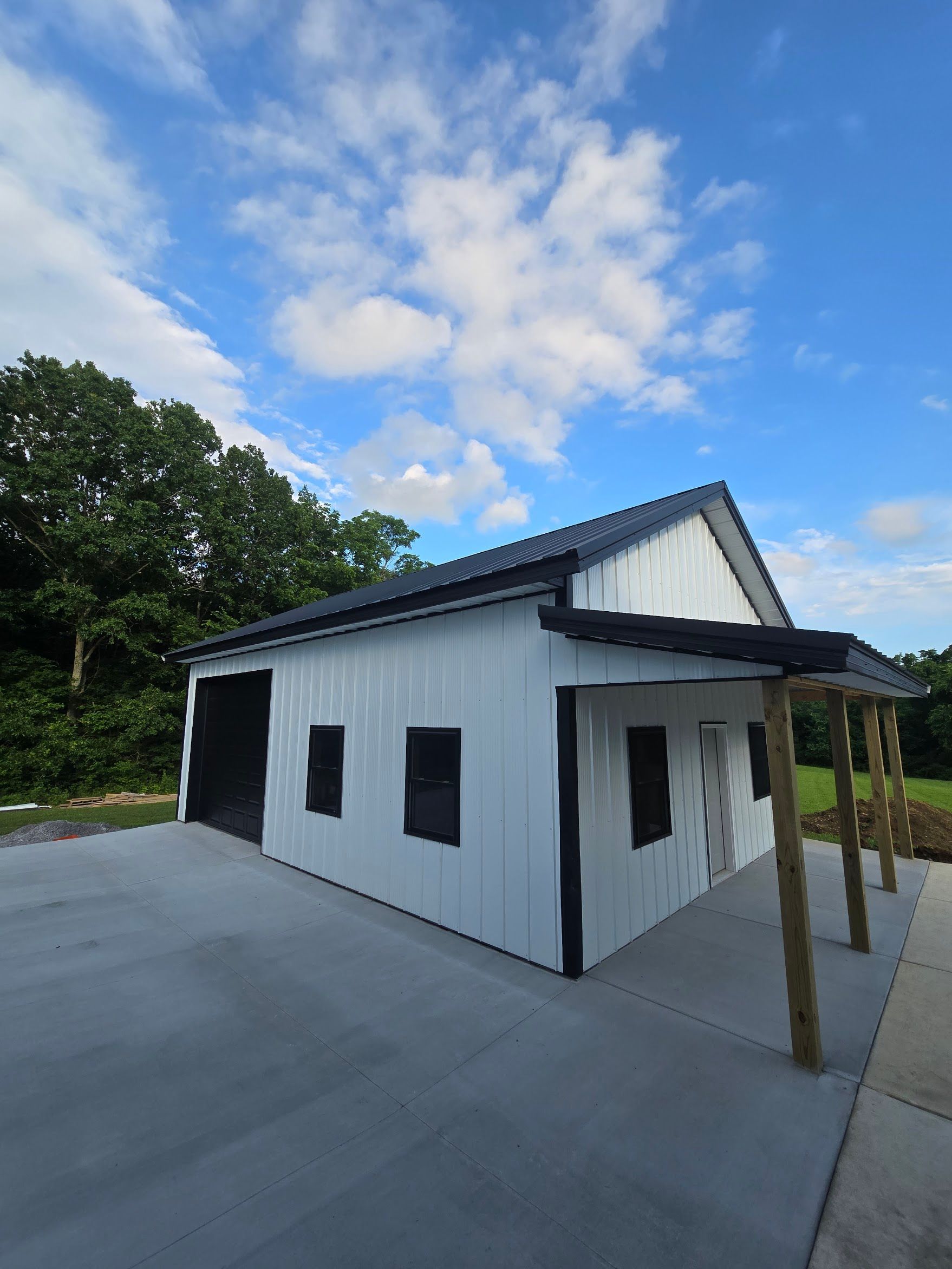 White building with black trim, black roof, and concrete slab under a blue sky