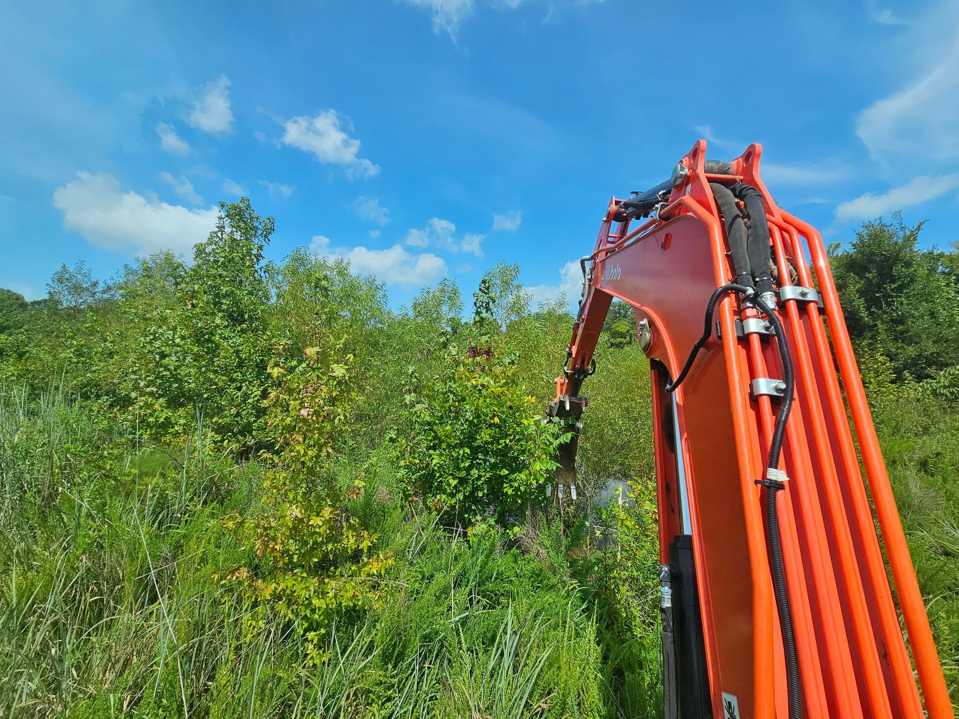 An orange excavator is sitting in the middle of a grassy field.
