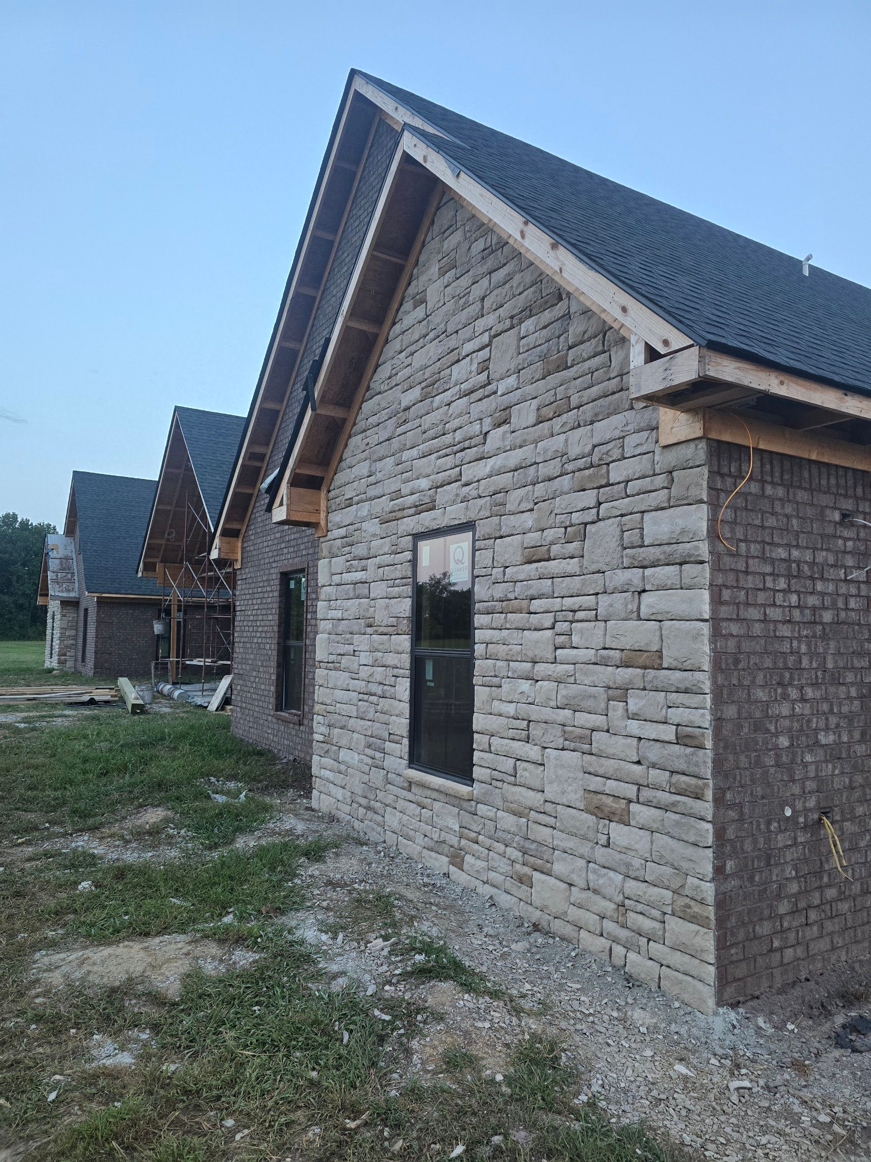 Stone-clad house exteriors under construction, with dark roof shingles and visible wooden framing