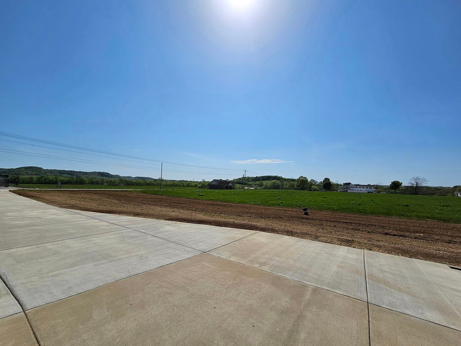 A concrete road leads to a field with a blue sky in the background.