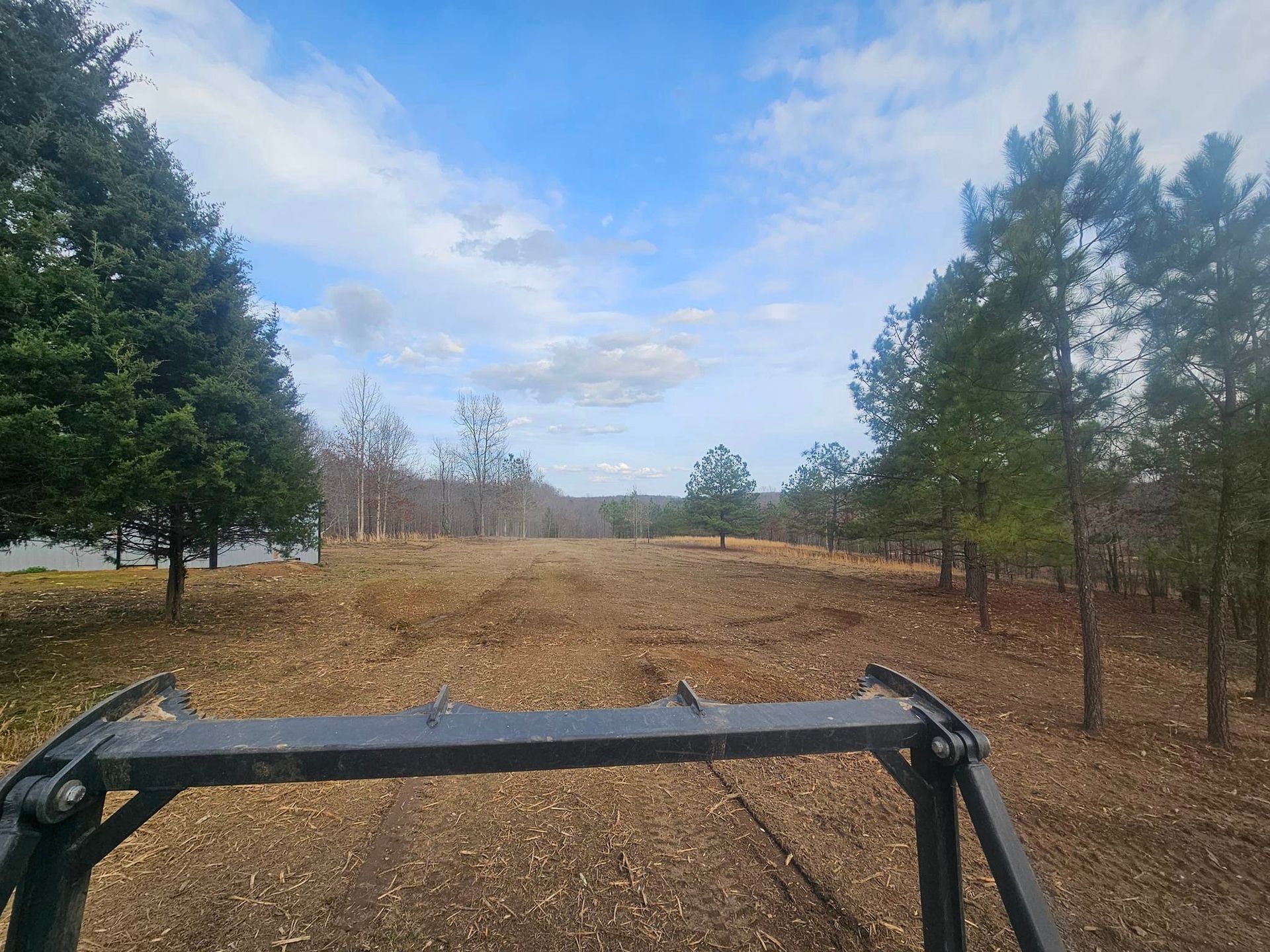 A tractor is driving down a dirt road in the woods.