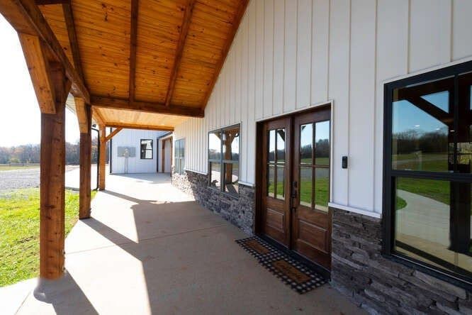 Covered porch with white siding, stone accents, and wooden door and beams