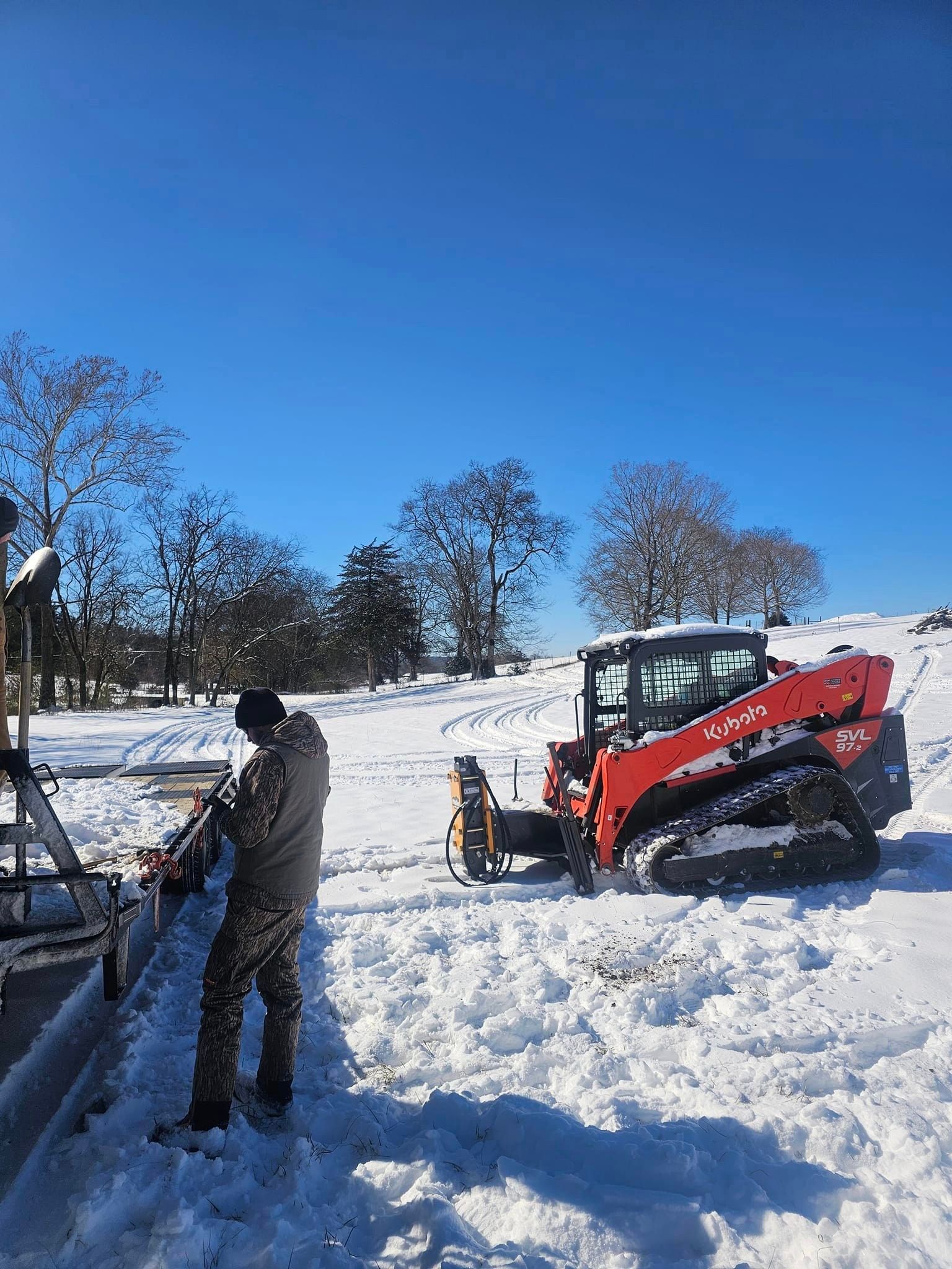 A man is standing in the snow next to a red tractor.