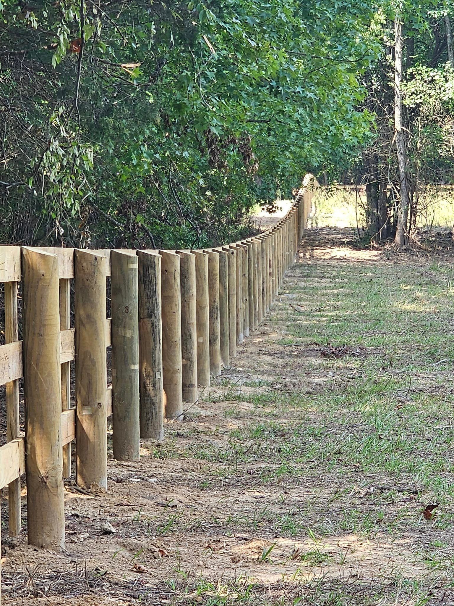 A wooden fence surrounds a grassy field in the woods.