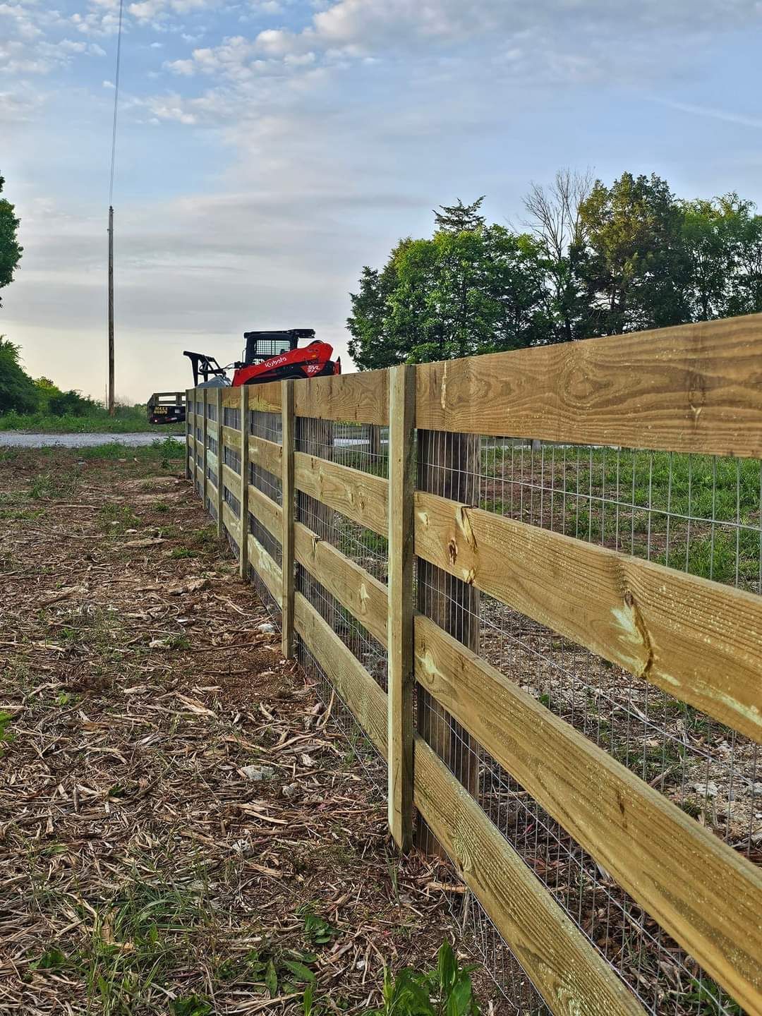 A wooden fence surrounds a field with a red tractor in the background.