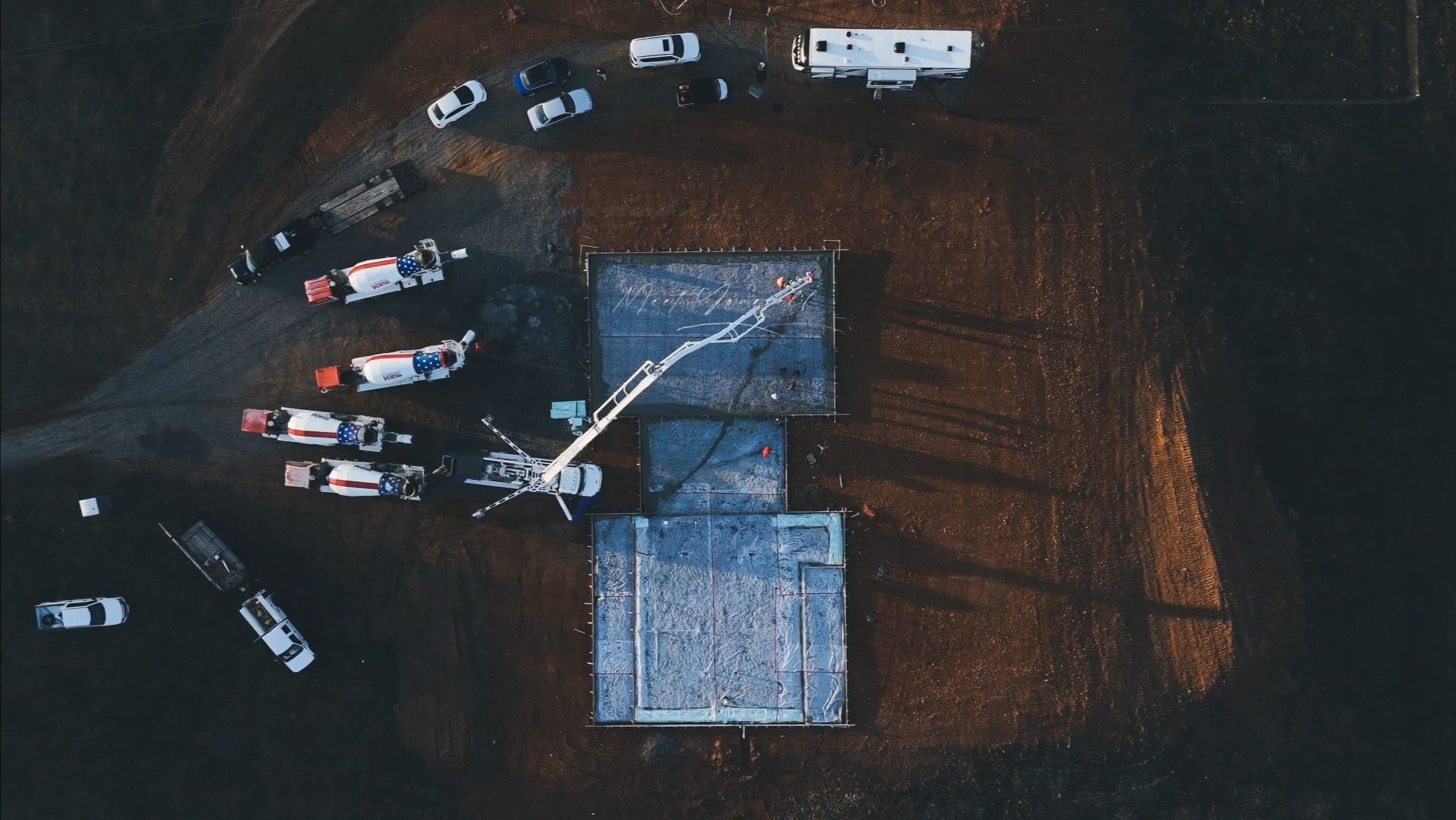 Overhead view of a helicopter spraying water on a building surrounded by emergency vehicles on brown terrain