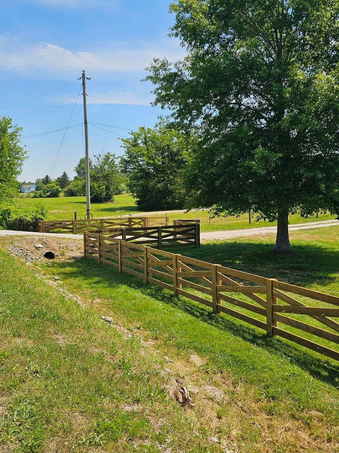 A wooden fence surrounds a grassy field with a tree in the background.