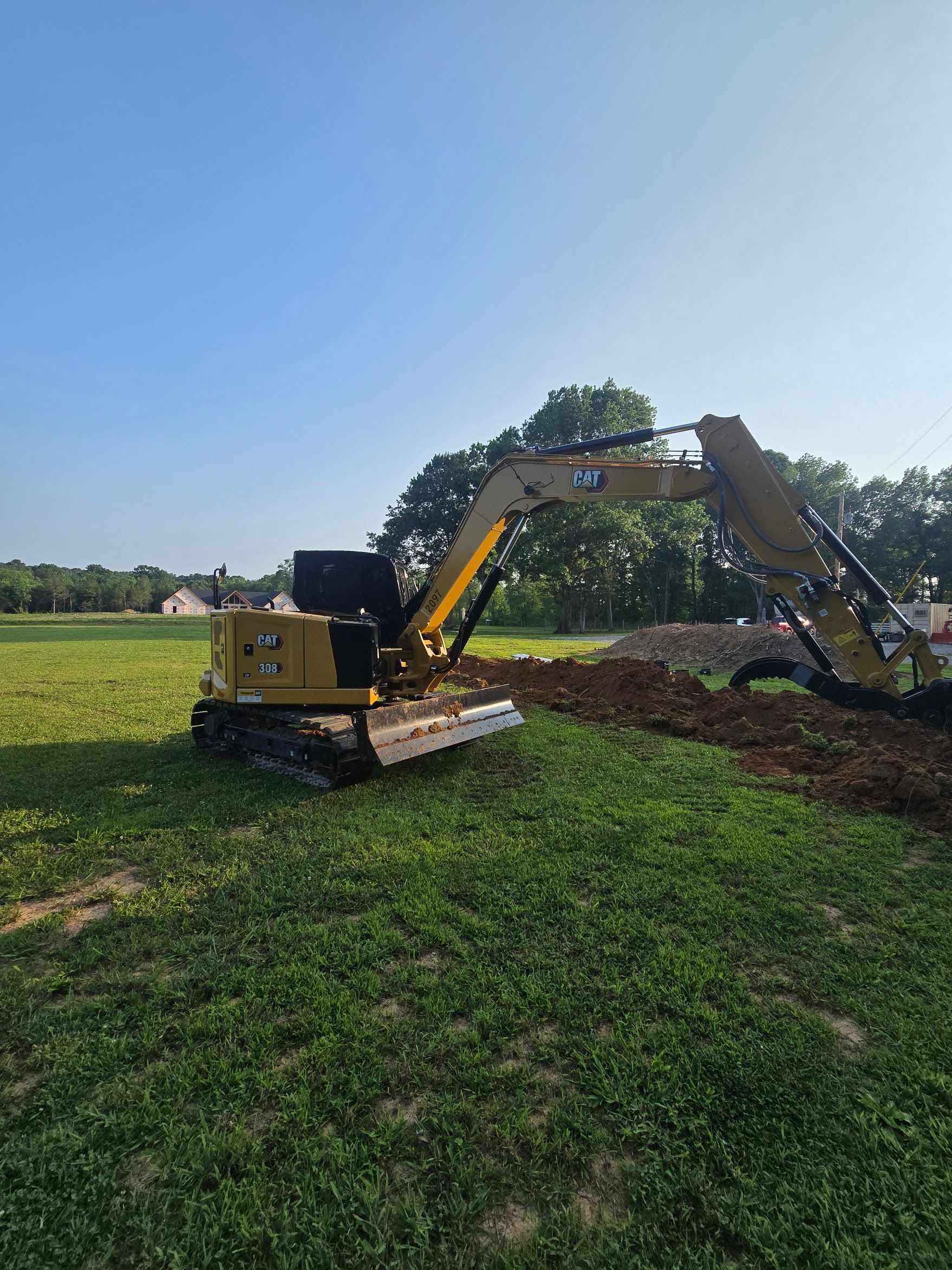 Yellow excavator digging in a grassy field on a sunny day