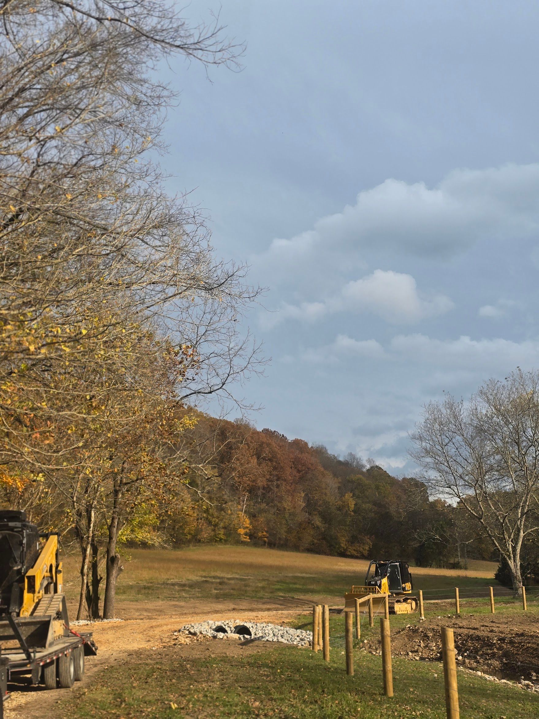Construction of a fence in a field with autumn trees and a cloudy sky