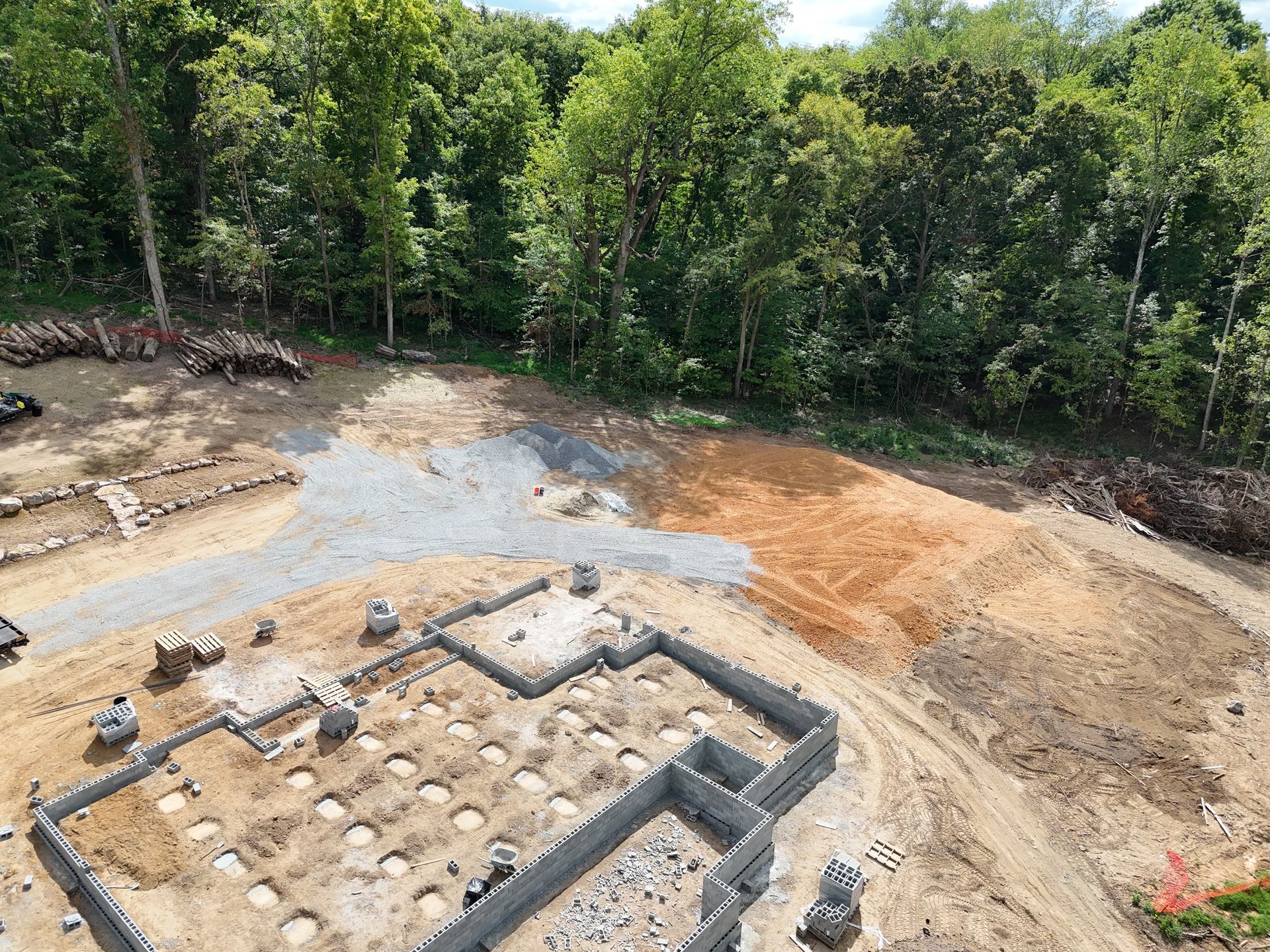 Aerial view of a construction site with a foundation, gravel path, and wooded area
