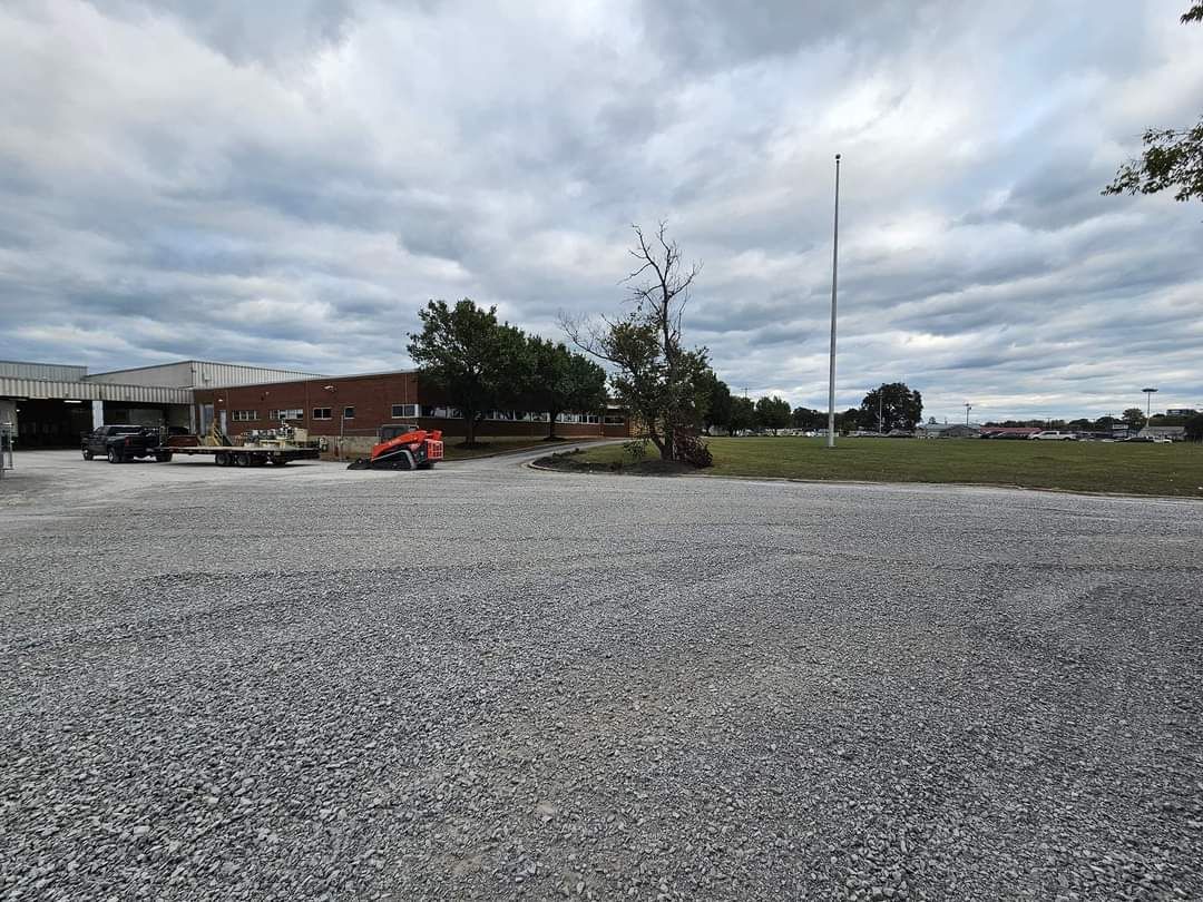 Gravel lot in front of a brick building and trees under a cloudy sky