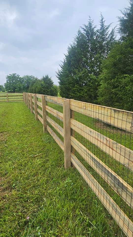 A wooden fence surrounds a grassy field with trees in the background.