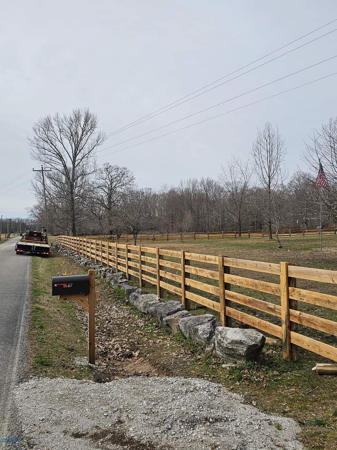 A wooden fence along the side of a road next to a mailbox.