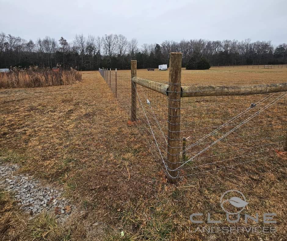 A wooden fence surrounds a field with trees in the background.