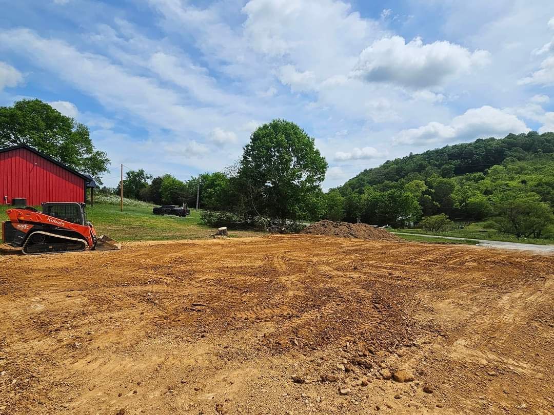 A large dirt field with a red barn in the background and a bulldozer in the foreground.