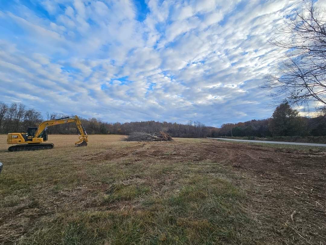 A yellow excavator is sitting in the middle of a field.
