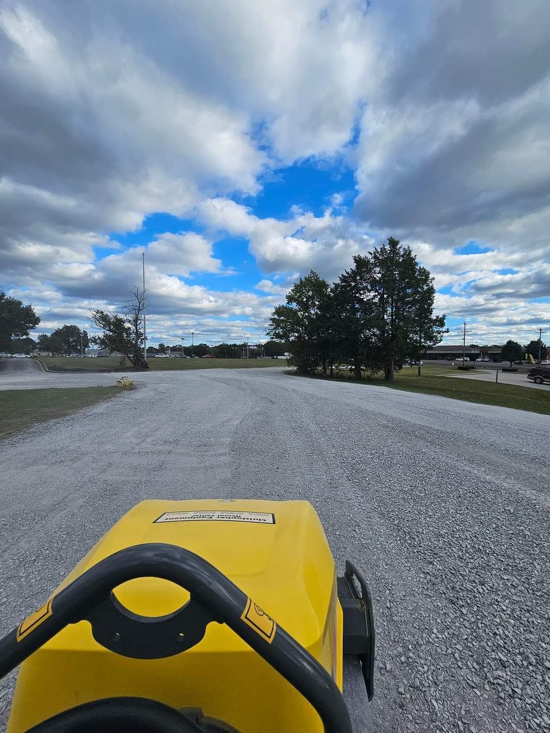 A yellow tractor is driving down a gravel road.
