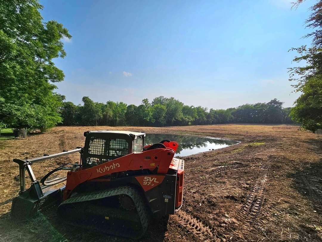 A bulldozer is driving through a muddy field next to a body of water.