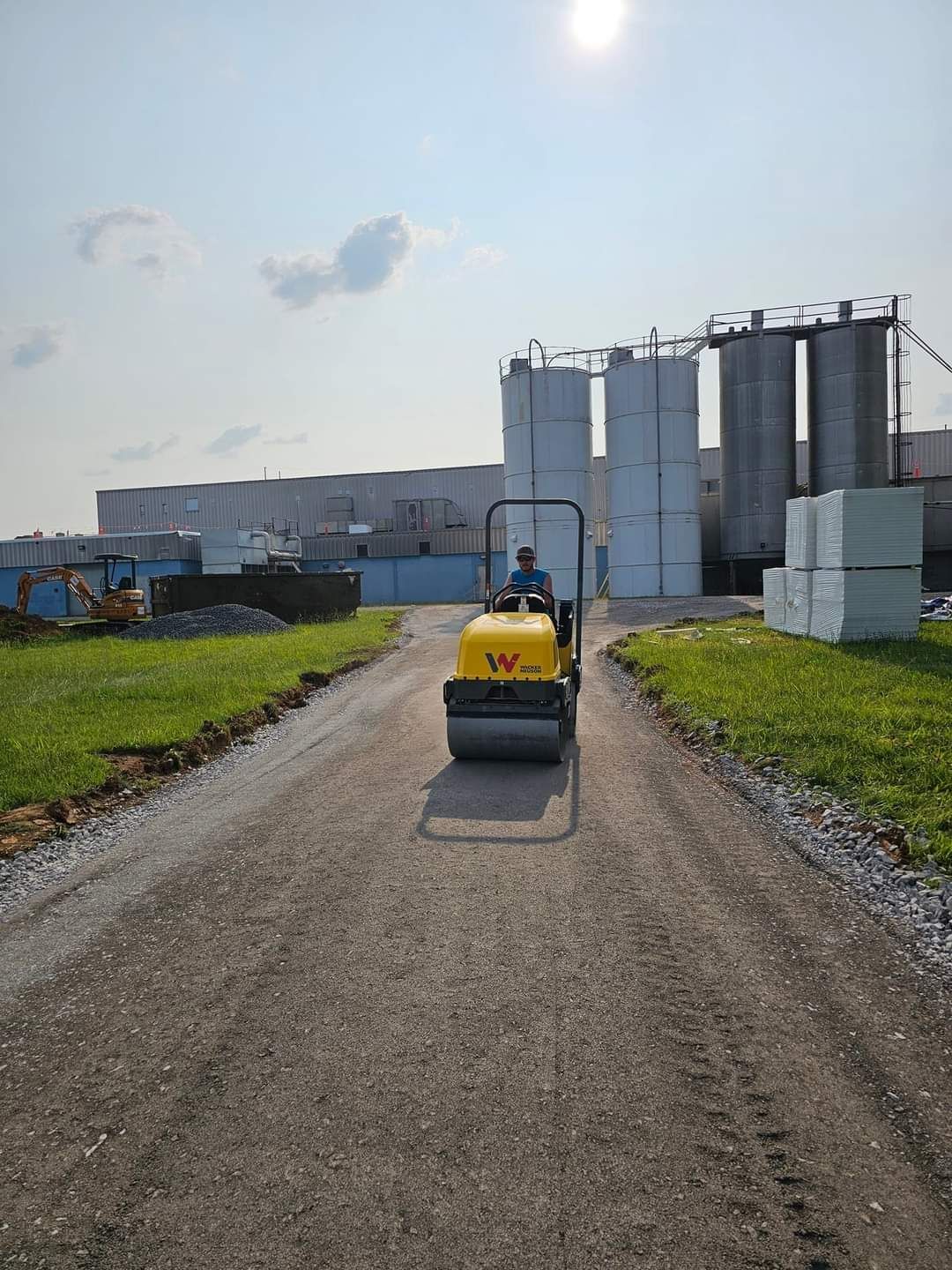 A man is driving a yellow roller down a dirt road.