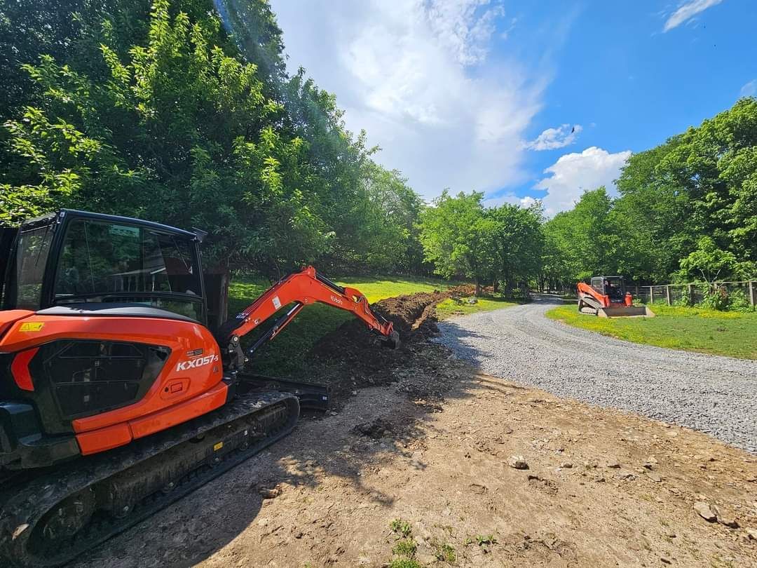 A large orange excavator is digging a hole in the middle of a dirt road.