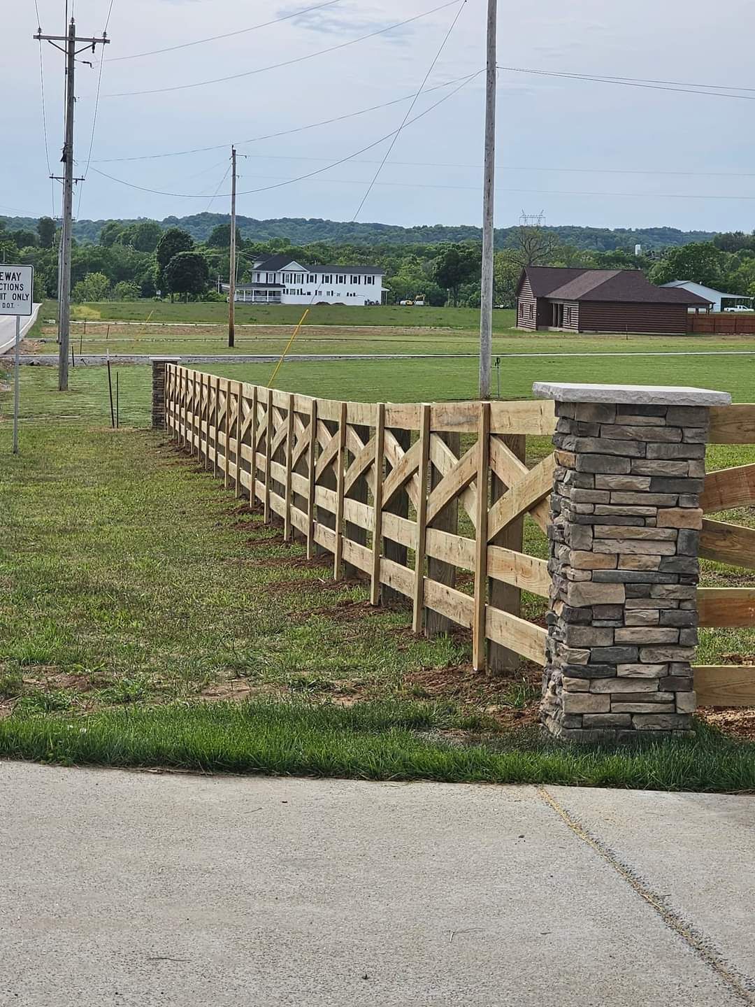 A wooden fence with a stone post in the middle of a grassy field.