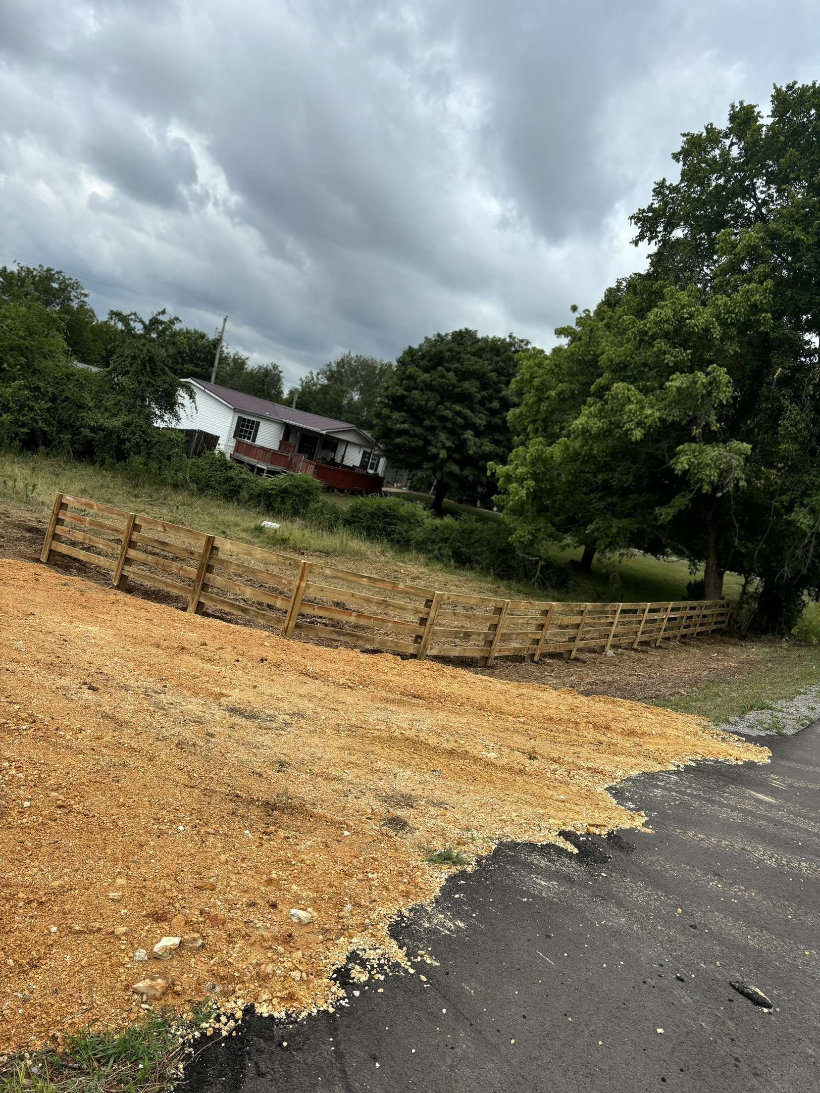 A pile of wood chips is sitting on the side of a road next to a wooden fence.