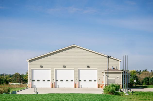 Beige garage building with three white doors under a blue sky, beside a grassy lawn