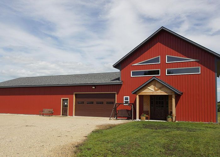 Red barn-style building with garage doors and a gravel driveway under a cloudy sky.