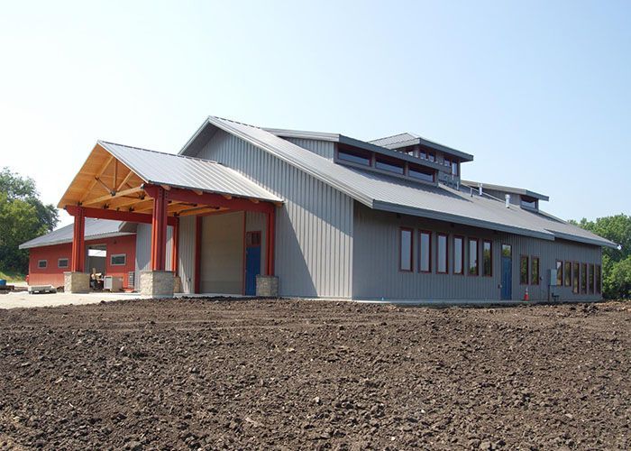 Modern building with gray metal roof and red entrance, viewed from a bare dirt lot.