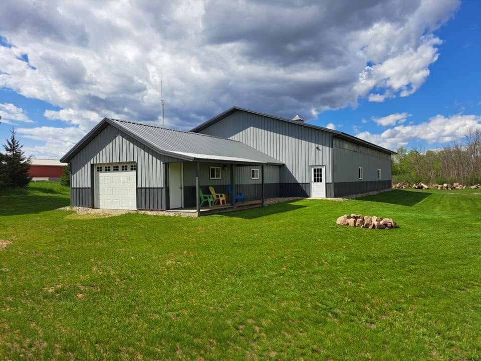 Gray metal barn-style house on a green lawn under a cloudy sky