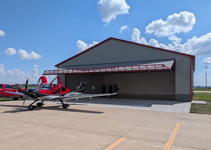 Red aircraft parked outside a large hangar under a blue sky with scattered clouds.