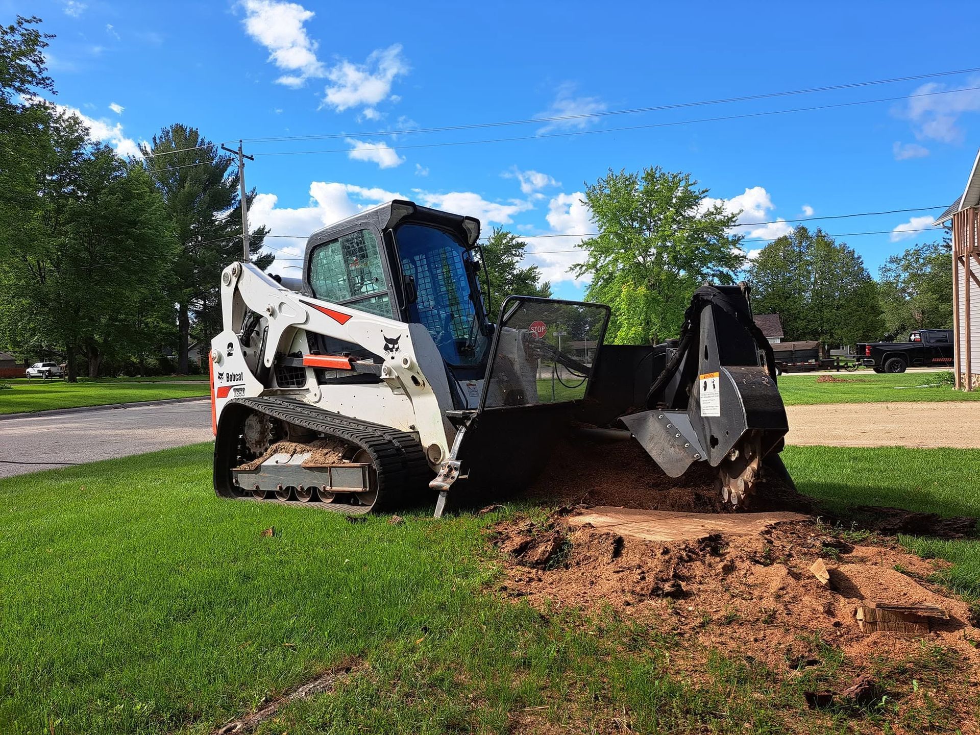 White skid-steer loader digging dirt in a grassy park under a blue sky