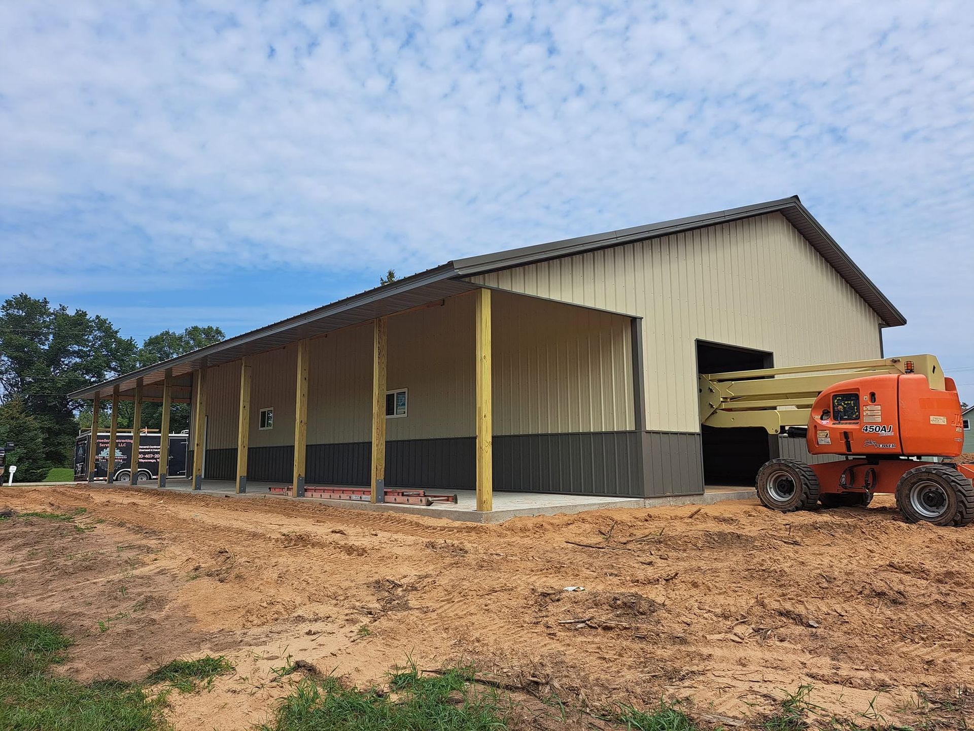 Large beige metal warehouse under construction, with an orange boom lift on a dirt lot.