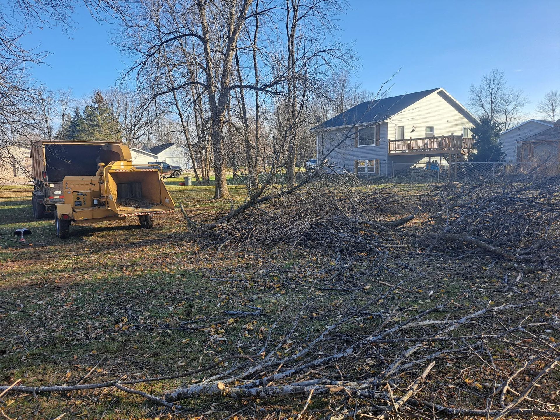 Yellow bulldozer clearing brush in a yard near a house on a sunny day