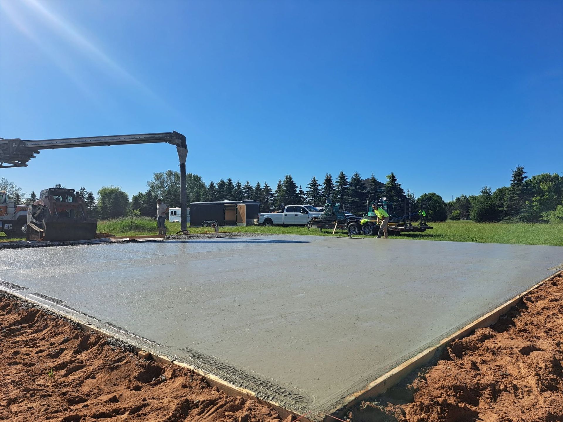 Freshly poured concrete slab at a construction site with workers under a blue sky