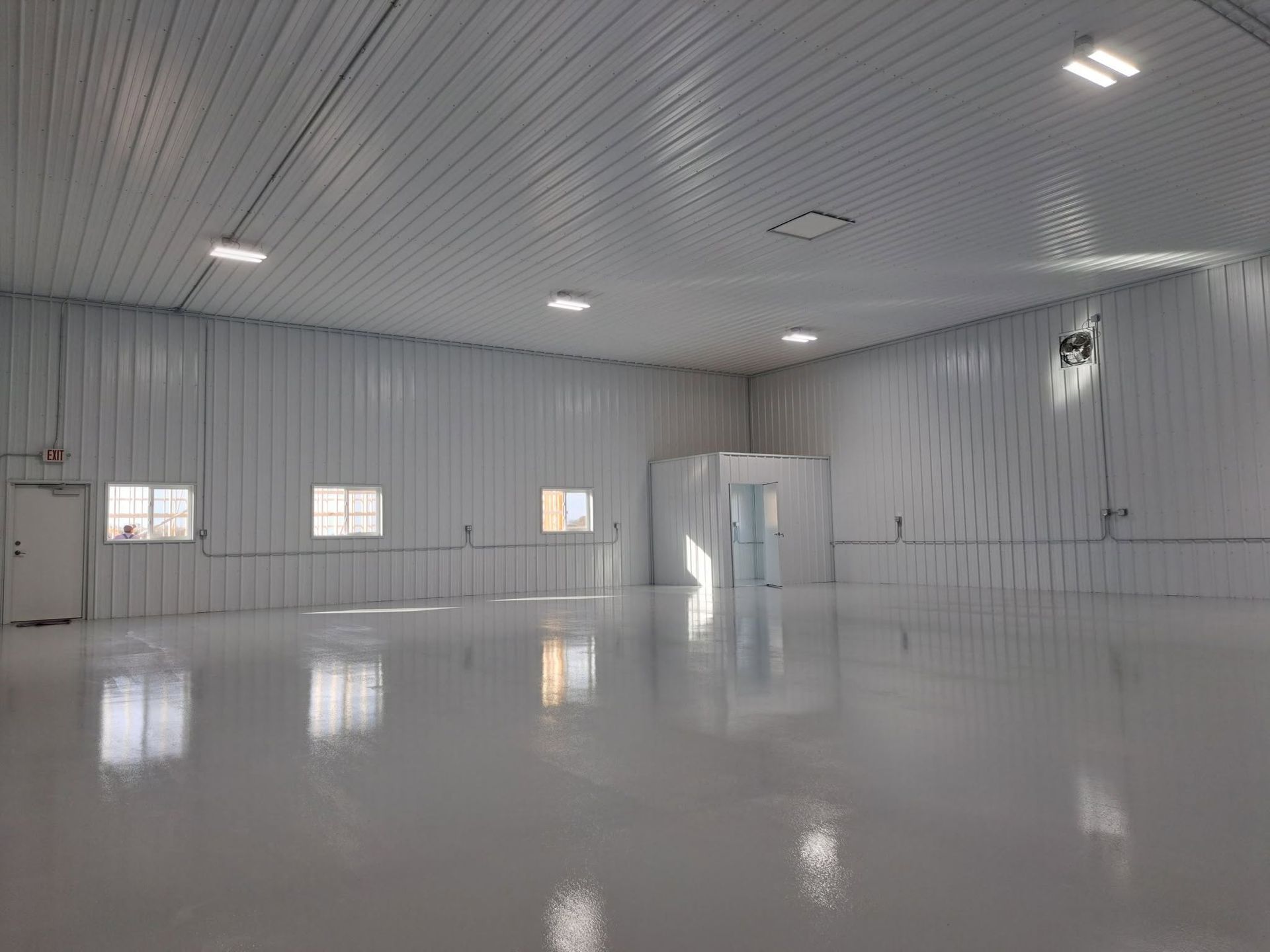 Empty white industrial room with glossy floor, metal walls, windows, and overhead lights