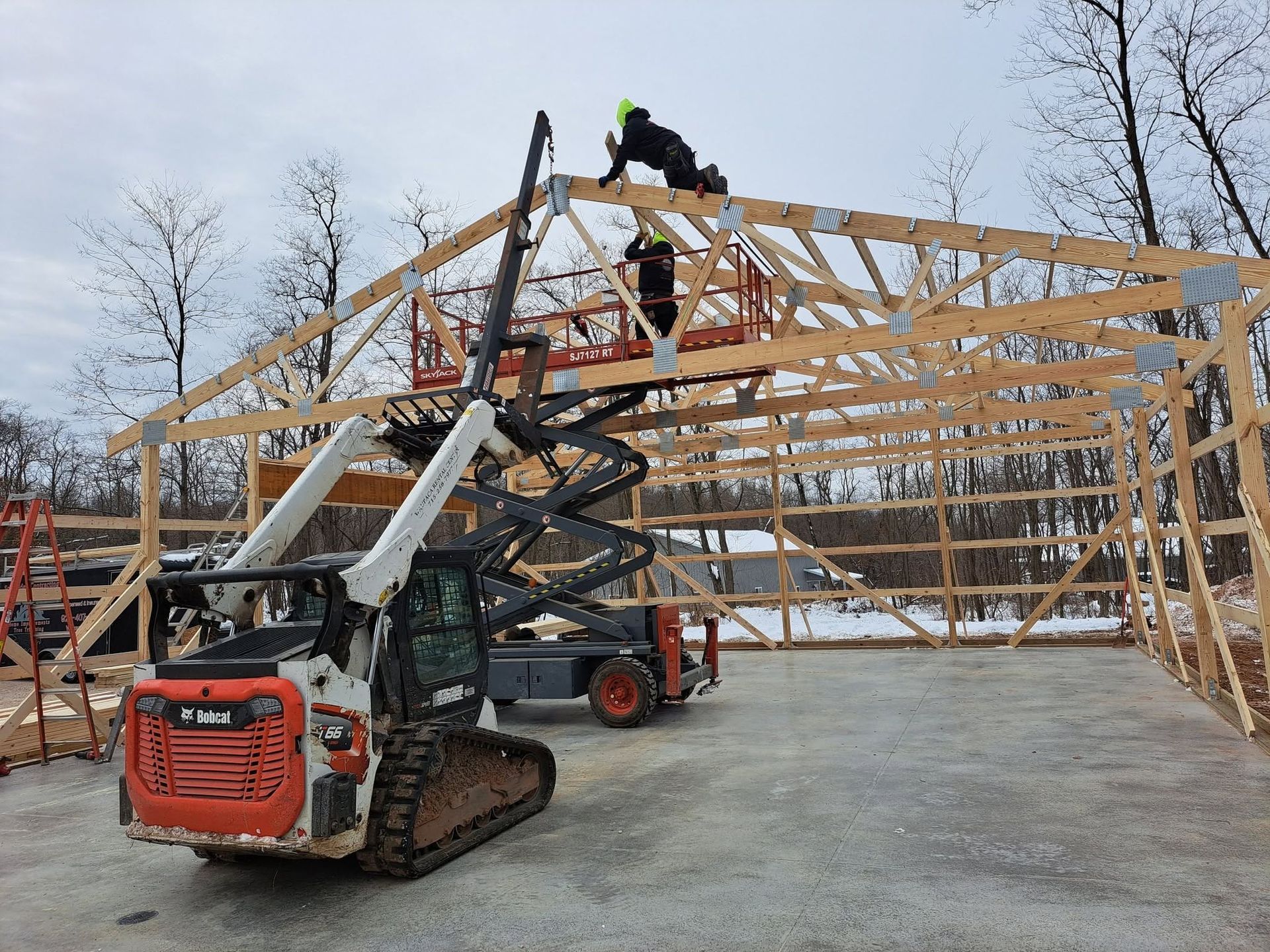 Workers installing wooden roof trusses with a skid steer at a house under construction