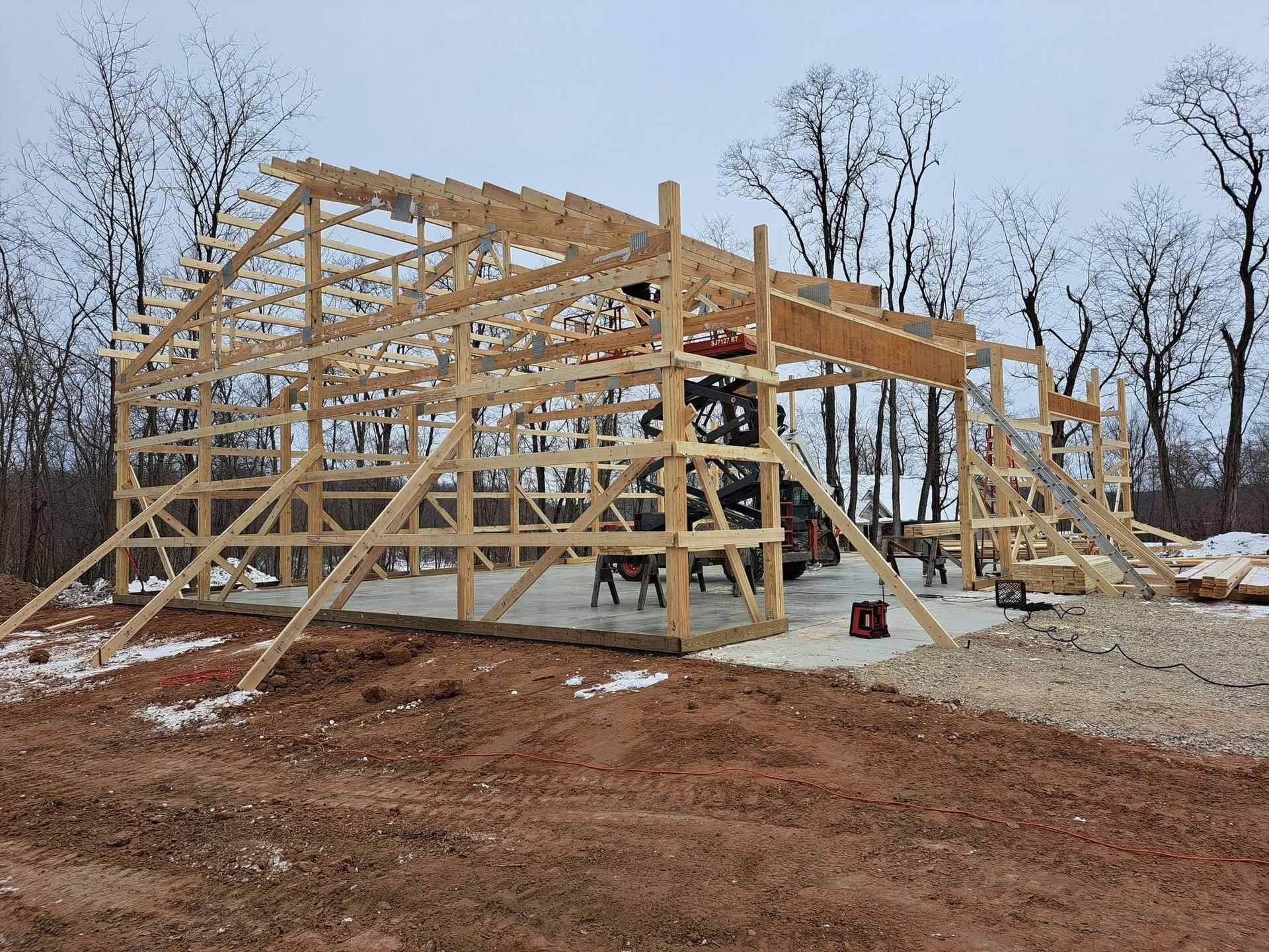 Wooden house frame under construction on a snowy, wooded lot.