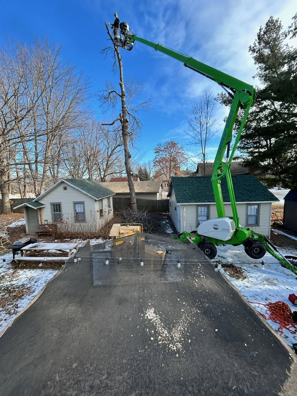 Green boom lift at a snowy house roofline, with workers near the chimney.