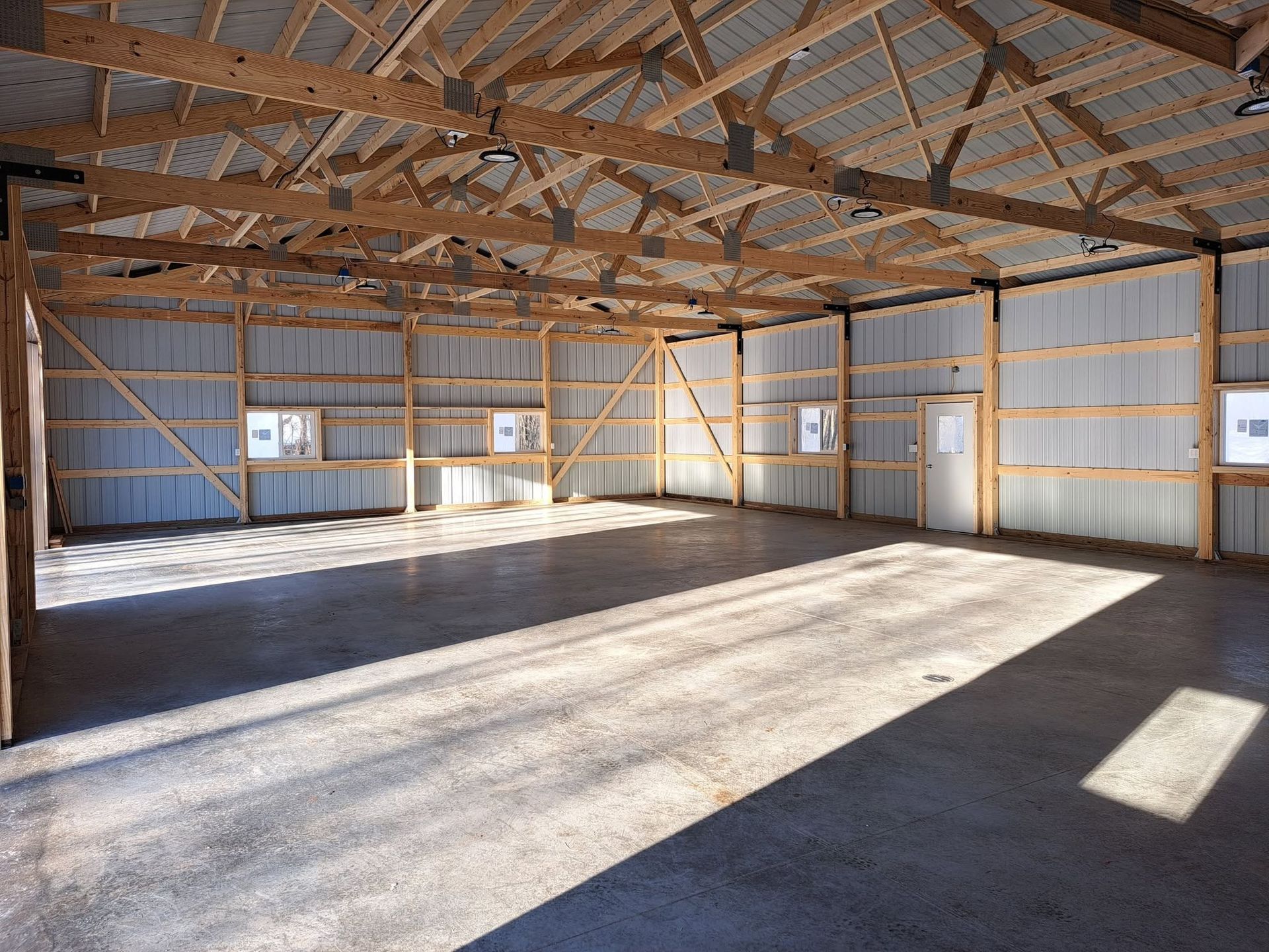 Empty wooden barn interior with exposed beams, metal walls, and sunlight streaming through windows.