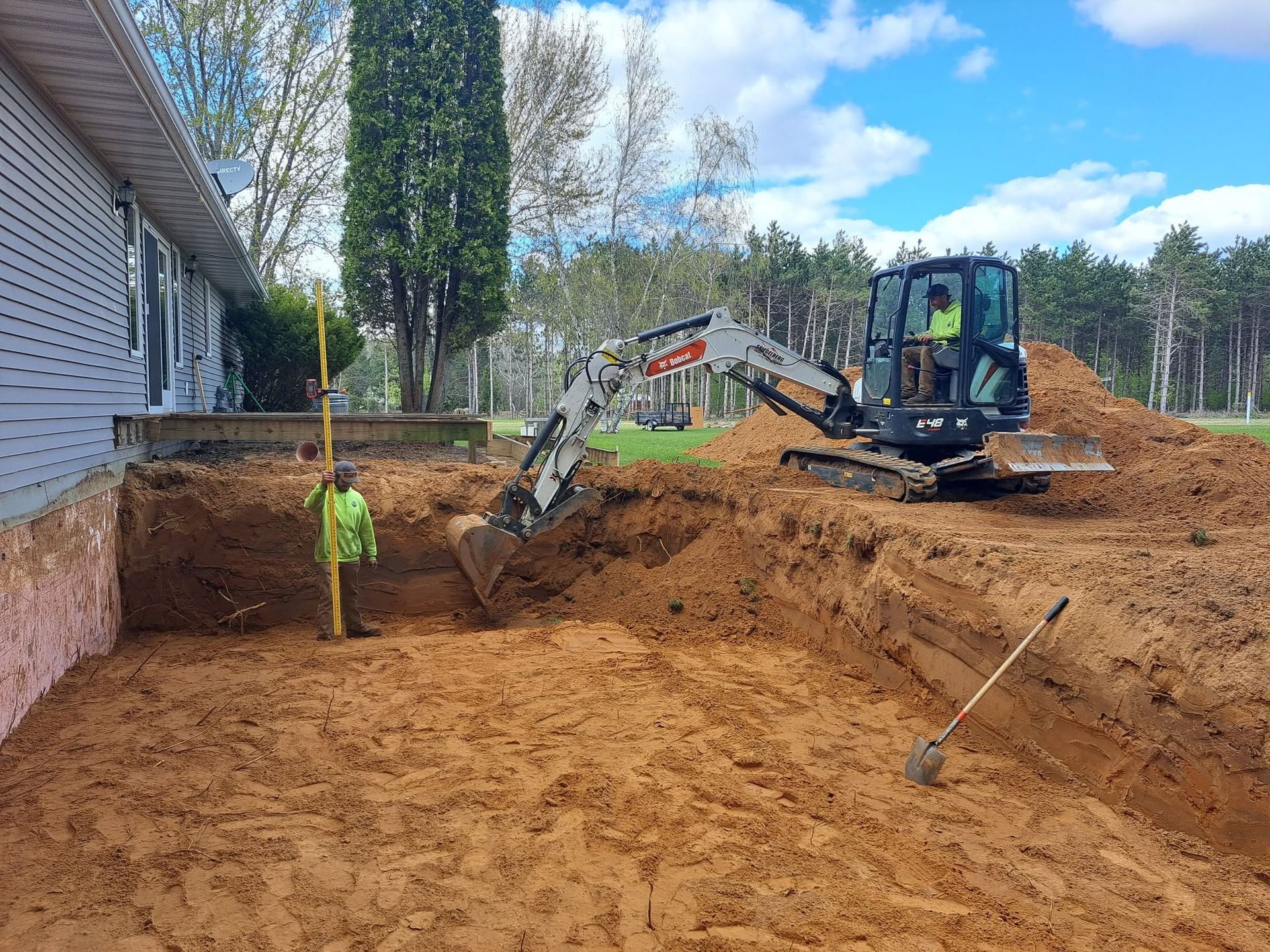 Backhoe excavating a dirt backyard beside a house on a sunny day